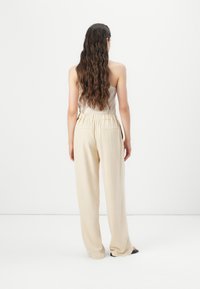 Pantaloni beige a gamba larga con cintura elastica, realizzati in tessuto liscio. Presentano due tasche posteriori e una vestibilità comoda lungo le gambe.