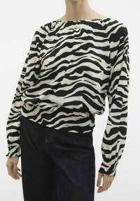 Blusa con stampa zebra in bianco e nero, con scollo rotondo, maniche lunghe, elastico in vita e texture del tessuto liscia. Indossata con jeans scuri.