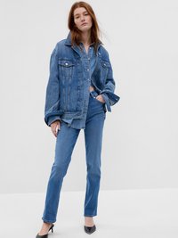 Veste en jean avec une coupe décontractée, couleur bleu clair, col pointu et boutons en métal, associée à un jean bleu assorti et des talons noirs.