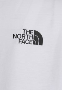 Bílý bavlněný tričko s černým logem zakřivených linií s nápisem "THE NORTH FACE" na levé straně. Hladký povrch, krátké rukávy.