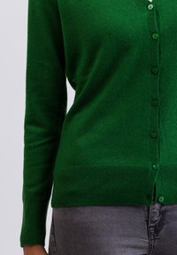 Grön stickad cardigan med långa ärmar, rund halsringning och en rad matchande knappar framtill. Mjuk textur och ribbad nederkant.