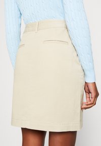 Knee-length beige skirt made of smooth fabric with a straight cut, featuring two back pockets and a clean hemline.