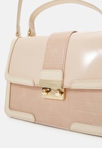 Sac à main rose présentant une combinaison de matériaux brillants et texturés, avec un fermoir doré, des coutures délicates et un design structuré.