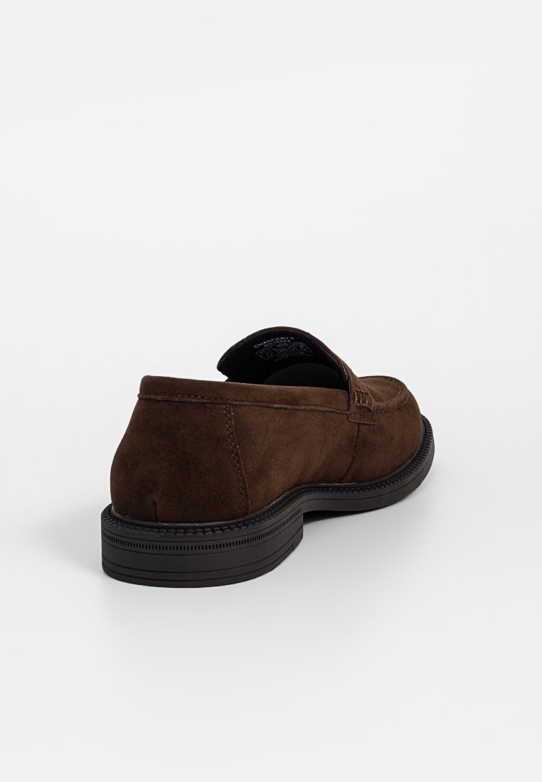 Mocasín de ante marrón con un perfil bajo y suela de goma. Presenta una costura a lo largo de los lados y una textura suave.