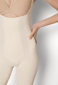 Beige shapewear featuring smooth, stretchy fabric, a cut-out back, and side ventilation holes, designed for a seamless fit.