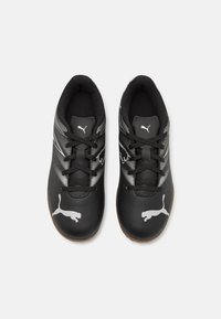 Zapatillas deportivas negras con parte superior sintética que presenta un logo de Puma plateado y patrones texturizados en blanco, puntera redonda y cordones negros.