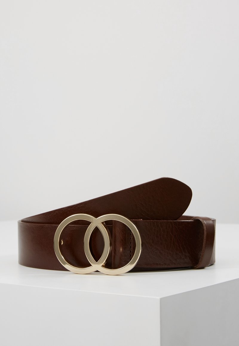 Ceinture en cuir marron foncé avec une boucle double anneau en or, présentée enroulée sur une surface blanche sur un fond uni.