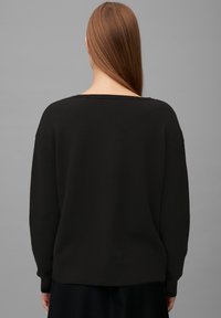 Schwarzer Strickpullover mit lockerem Schnitt, weitem Ausschnitt und langen Ärmeln. Strukturierter Stoff und gerippte Saumdetails am unteren Ende.