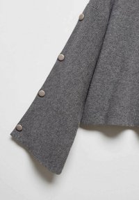 Manche en tricot côtelé gris avec large évasement et quatre boutons ronds gris le long du bord extérieur, suspendue sur un fond blanc.