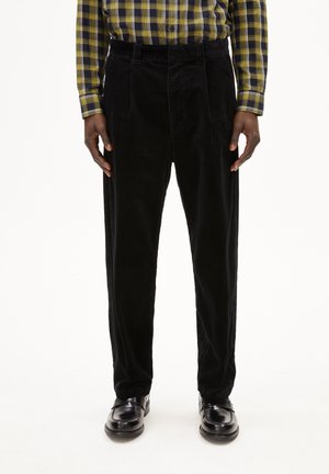 Zwarte corduroybroek met een losse fit, met plooien aan de voorkant en een gestructureerde stof. Gecombineerd met zwarte nette schoenen en een geruite overhemd.