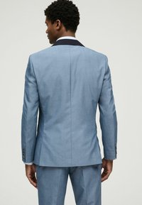Hele halli ülikonna jakki musta kaelusega, ühe ventiiliga ja peene tekstuuriga. Slim-fit disain, nööpidega varrukatel, tagant vaade.