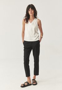Haut sans manches en satin blanc, pantalon noir ajusté et sandales noires avec des accessoires en or. Design simple et textures lisses.