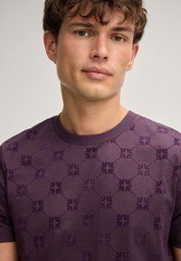 Lila gestricktes T-Shirt mit einem strukturierten Muster aus ineinandergreifenden Kreisen und floralen Motiven, mit Rundhalsausschnitt und kurzen Ärmeln.