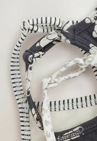 Säädettävät kangasnauhat musta-valkoisilla kuvioilla ja muovirenkaalla varustetut kiinnitykset vaalealla taustalla.