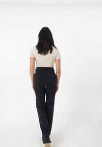 Jeans negros de cintura alta con un diseño de pierna recta, que cuentan con dos bolsillos traseros y un dobladillo limpio. Combinados con una blusa ajustada color beige claro.
