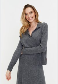 Pull en laine gris avec un col en V et des manches longues, doté d'un ourlet côtelé. Comprend un petit détail de logo rouge. Texture douce.
