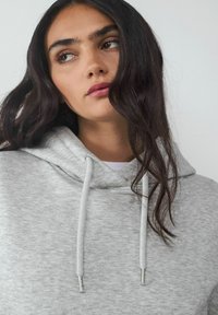 Szary sweatshirt z miękkiej, teksturowanej tkaniny. Posiada kaptur ze sznurkiem i metalowymi końcówkami. Prosty fason z luźnym krojem.