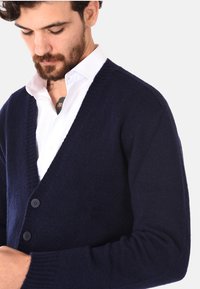 Cardigan navy realizzato in tessuto morbido, con scollatura a V, bordi a coste e due bottoni sul fronte, che offre una silhouette rilassata.