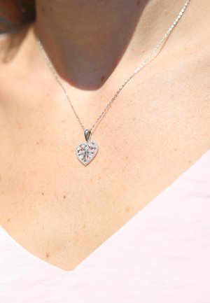 Zilveren hartvormige pendant met een verfijnd boomontwerp, omringd door kleine heldere stenen, bevestigd aan een delicate ketting.