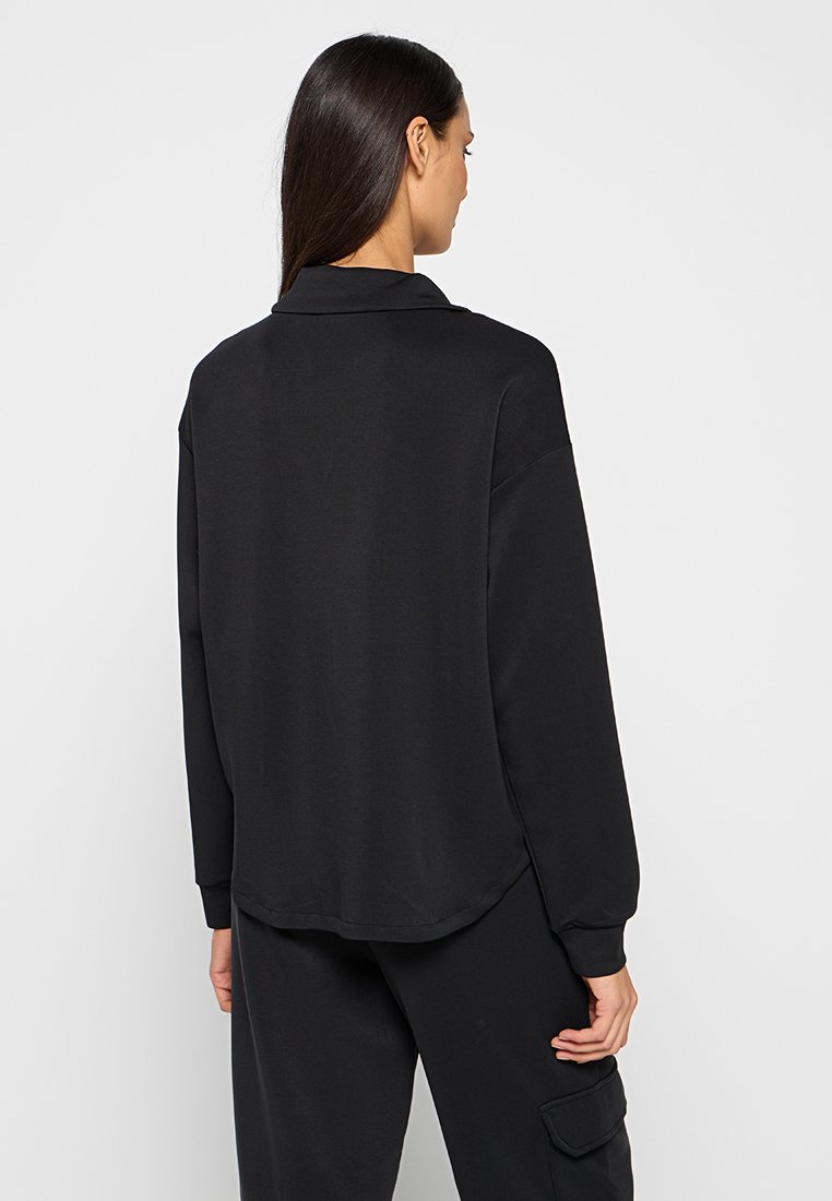 Schwarzes Langarmhemd mit Kragen, entspannter Schnitt und abgerundetem Saum. Weicher Stoff mit minimalen Details.