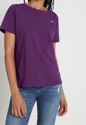 Purple cotton t-shirt with short sleeves and a round neckline. Features a small logo on the chest and is paired with distressed blue jeans.