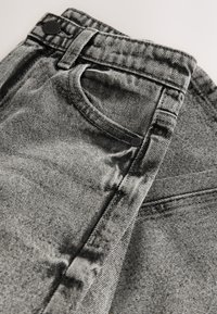 Grijze spijkerbroek met een klassiek ontwerp van vijf zakken, een ritssluiting en zwarte hardware. De stof heeft een lichte textuur en een vervaagde afwerking.