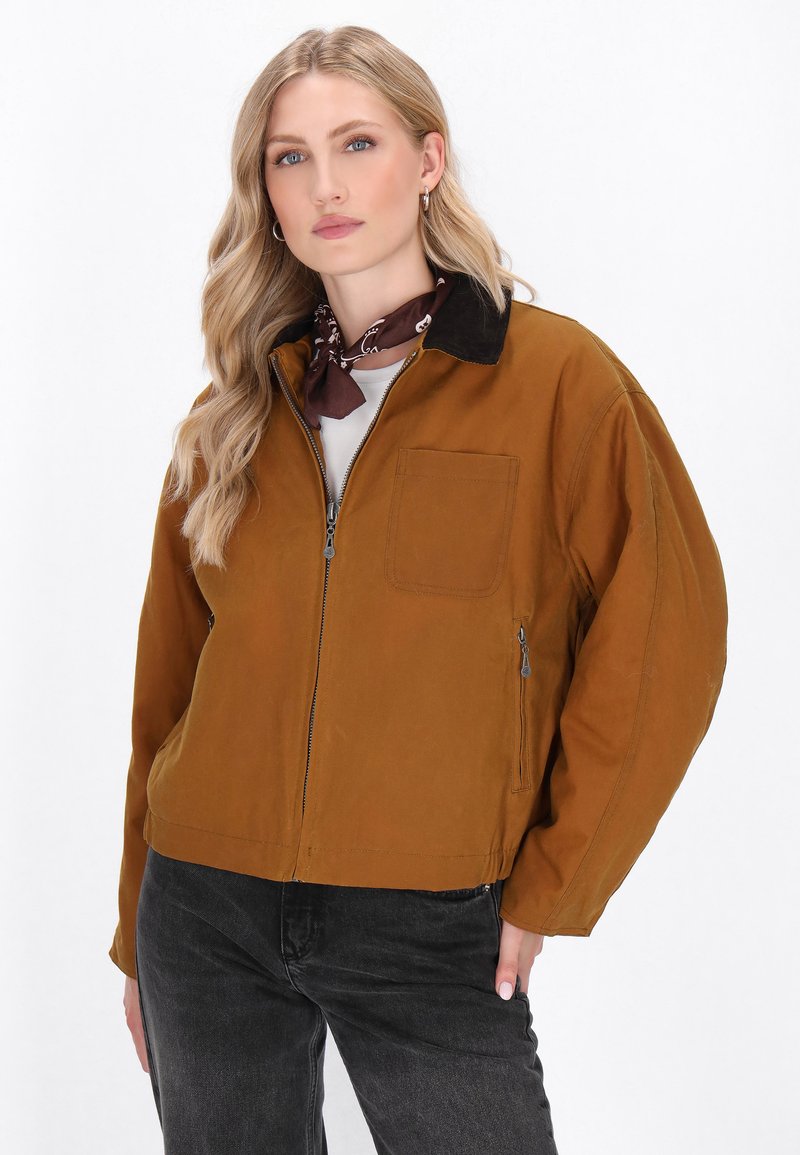 Een brown utility jack met een ritssluiting aan de voorkant, een borstzak en een contrasterende zwarte kraag. Draagt over een grijs shirt met een lichte textuur.