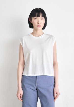 White sleeveless crop top with a round neckline, made of smooth fabric. Paired with light blue high-waisted jeans.