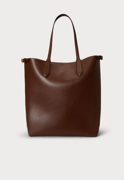 Brūna ādas plecu soma ar diviem pagarinātiem rokturiem, gluda tekstūra, minimālistisks dizains un smalkas detaļas rokturu piestiprinājumā.