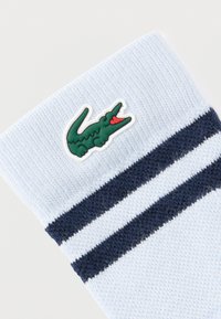 Ανοιχτό μπλε πλεκτό κάλτσα με δύο σκούρες μπλε οριζόντιες ρίγες και ένα πράσινο λογότυπο κροκόδειλου κοντά στη μανσέτα.