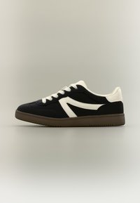 Μαύρο και άσπρο αθλητικό παπούτσι από σουέντ και ύφασμα, με ρετρό σχεδιασμό, στρογγυλή μύτη, λευκά κορδόνια και καφέ λαστιχένια σόλα.