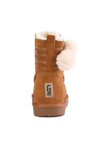 Botas de tobillo de ante marrón con un suave forro de piel, que cuentan con una lengüeta trasera, pompones decorativos y detalles de costura horizontal.