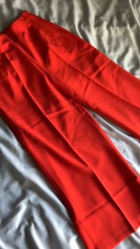 Červené široké kalhoty vyrobené z hladkého materiálu, s plochým pasem a uvolněným, volným designem. Žádné viditelné vzory nebo akcenty.