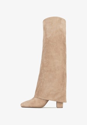 Hoher, beiger Wildlederstiefel mit niedrigem Blockabsatz und abgerundeter Spitze, vor weißem Hintergrund dargestellt.