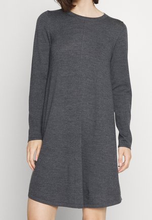 Mujer con un vestido de punto de manga larga hasta la rodilla, de color gris oscuro, con escote redondo y sutiles detalles de costuras verticales.