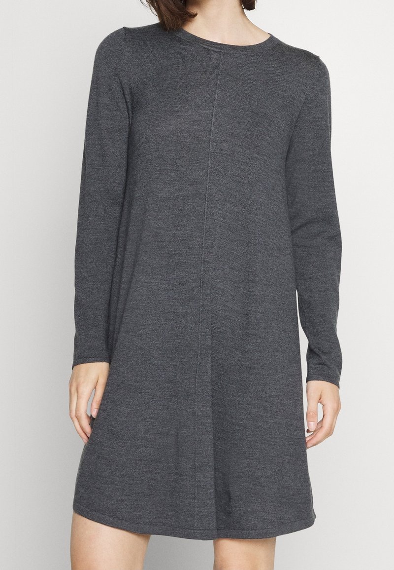 Femme portant une robe en maille gris foncé, à manches longues, longueur genoux, avec un col rond et des détails subtils de coutures verticales.