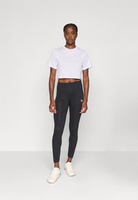 Lila cropped póló, fekete, magas derekú leggings és világos sportcipők. Az outfitt sima textúrával és testhezálló kialakítással rendelkezik.
