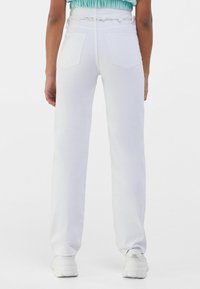 Pantalones blancos de cintura alta con cintura deshilachada, dos bolsillos traseros y un diseño de pierna recta. Tejido texturizado con un acabado suave.