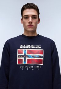 Sudadera navy con cuello redondo que presenta un diseño geométrico multicolor central y texto. Tejido suave con cuello acanalado oscuro.