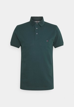 Polo vert foncé à manches courtes avec col et trois boutons, présentant un petit logo rouge, blanc et bleu sur la poitrine gauche.