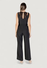 Mono negro con un cuerpo ajustado y piernas acampanadas. Presenta un detalle de encaje en la espalda con un agujero en forma de llave y cierre de cremallera. Textura elegante y suave.