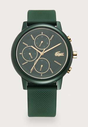 Montre verte avec un cadran rond texturé, des accents dorés, trois sous-cadrans et un bracelet en silicone texturé vert. Logo Lacoste présent sur le cadran.