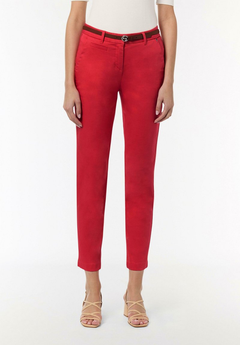 Rote maßgeschneiderte Hose mit glatter Oberfläche, schmal zulaufendem Bein und einem braunen Gürtel mit rundem Verschluss. Trägt dazu nude-farbene Riemchenhighheels.