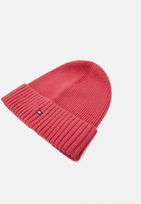Caciulă tricotată de culoare roz aprins, cu o margine ribbandă. Are un mic logo brodat în albastru, roșu și alb pe față. Textură moale.