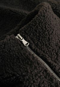 Primo piano di un tessuto in pile nero e testurizzato con una cerniera in metallo argento parzialmente aperta.