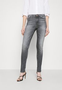 Jeans ajustados grises con un lavado desgastado, con cierre de cremallera, trabillas para el cinturón y sutiles detalles de costura. Combinados con tacones negros de tiras.