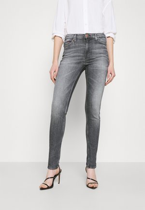 Jeans ajustados grises con un lavado desgastado, con cierre de cremallera, trabillas para el cinturón y sutiles detalles de costura. Combinados con tacones negros de tiras.