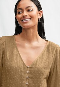 Braune, strukturierte Bluse mit tiefem V-Ausschnitt, Puffärmeln und Knopfleiste vorne. Verfügt über ein dezentes gepunktetes Muster für zusätzliche Details.