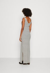 Robe maxi rayée en tricot noir et blanc. Dotée d'un dos en scoop et d'une fente sur le côté. Texture lisse avec une coupe ajustée.
