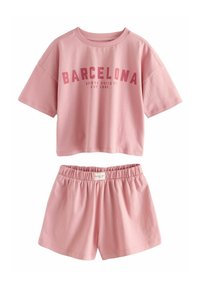 Ensemble loungewear en coton rose comprenant un haut court à manches courtes avec le texte "BARCELONA" et un short à taille élastique. Texture douce et design simple.